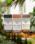 Tints of Nature Henna Cream True Black, Golden Brown and Dark Brown cartons placed on a wooden log with leaves surrounding