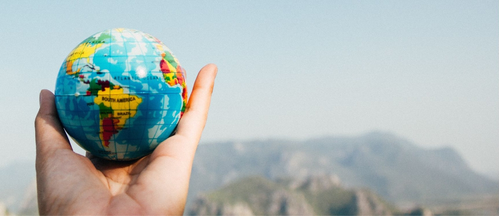 Hand holding up a globe with a mountain in the background 